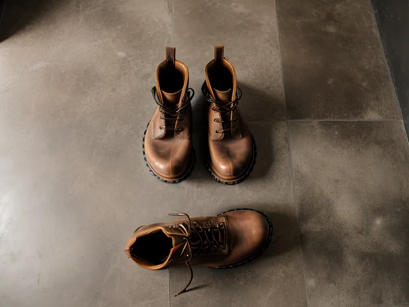 Leather work boots on bathroom floor beside topical nail supplement bottle